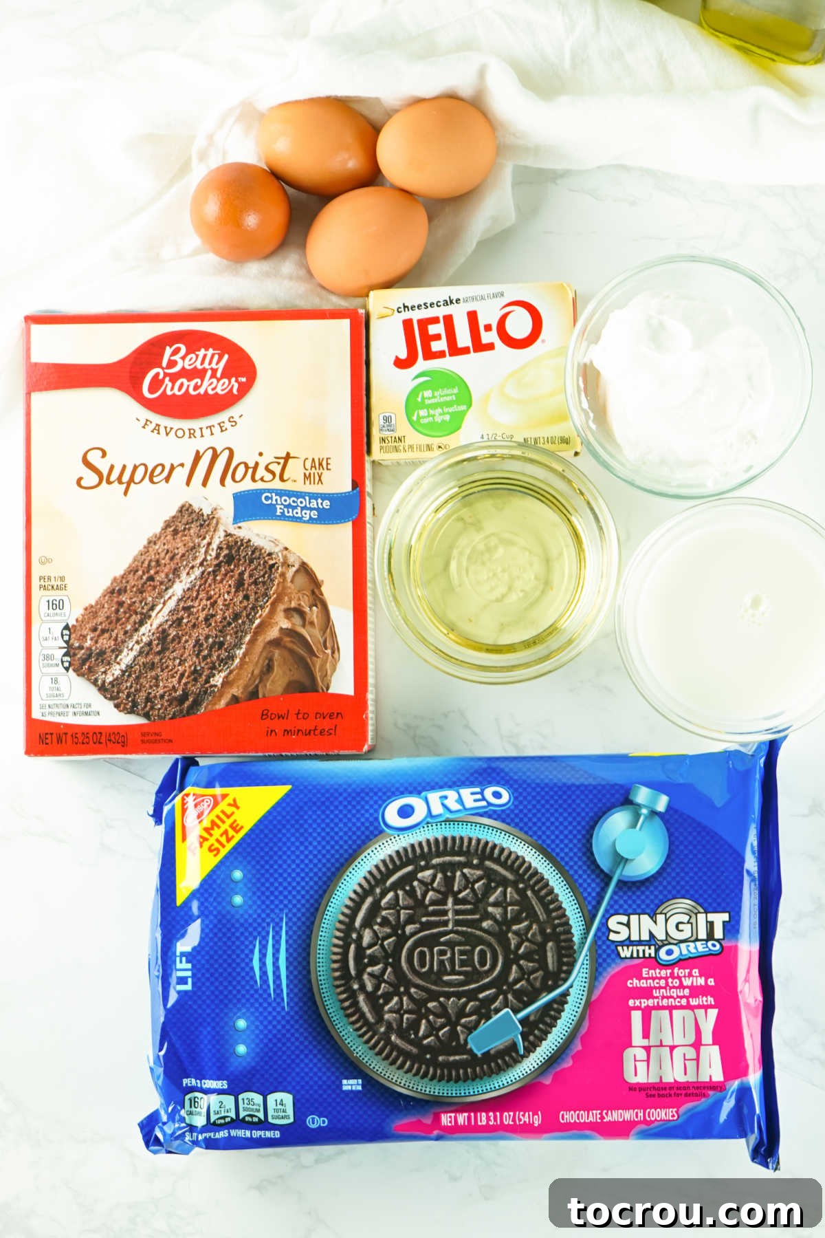 Hole-y Oreo Heaven 3 Essential ingredients laid out for making the chocolate Oreo poke cake, including a chocolate cake mix, eggs, milk, oil, and a stack of Oreo cookies.