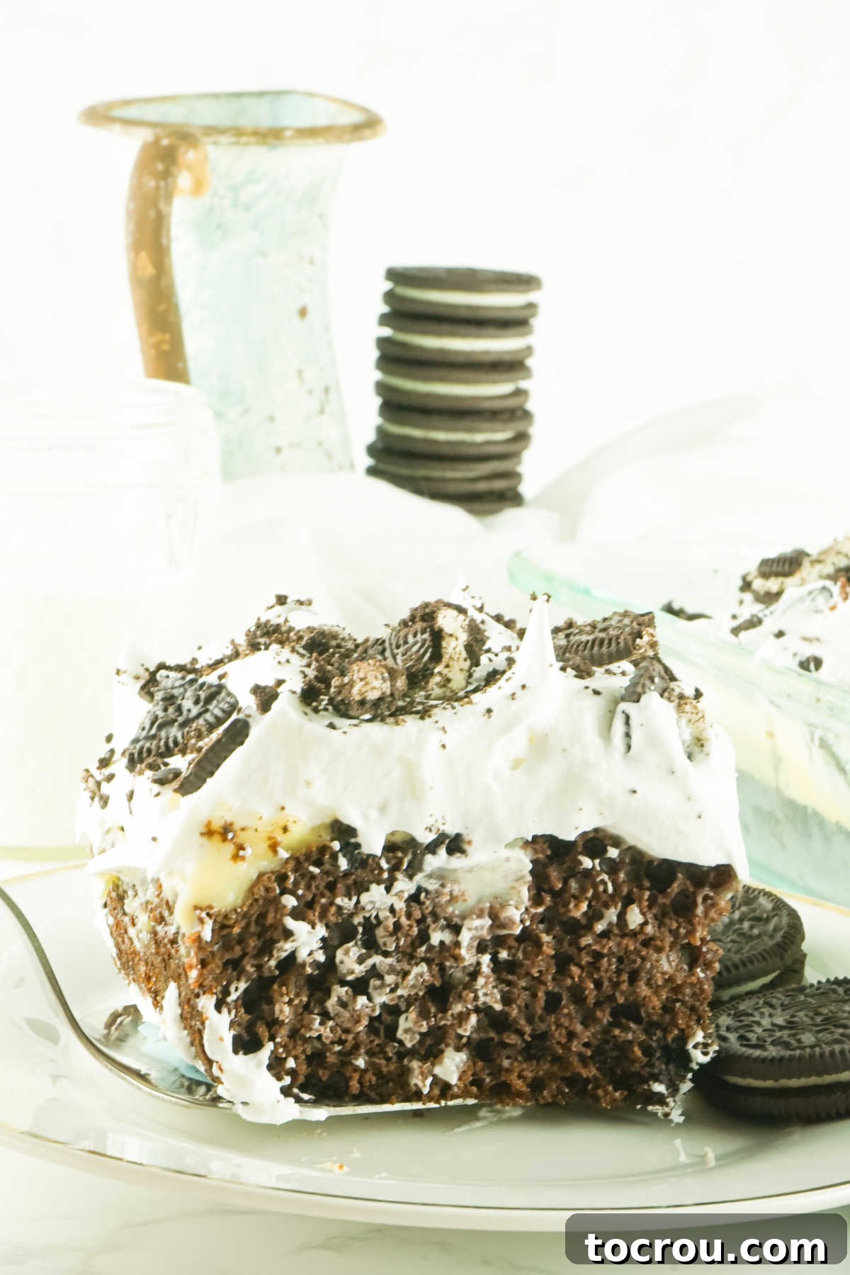 Hole-y Oreo Heaven 10 A hand gently placing a beautifully sliced piece of chocolate poke cake onto a white plate, ready to be enjoyed as a delightful dessert.