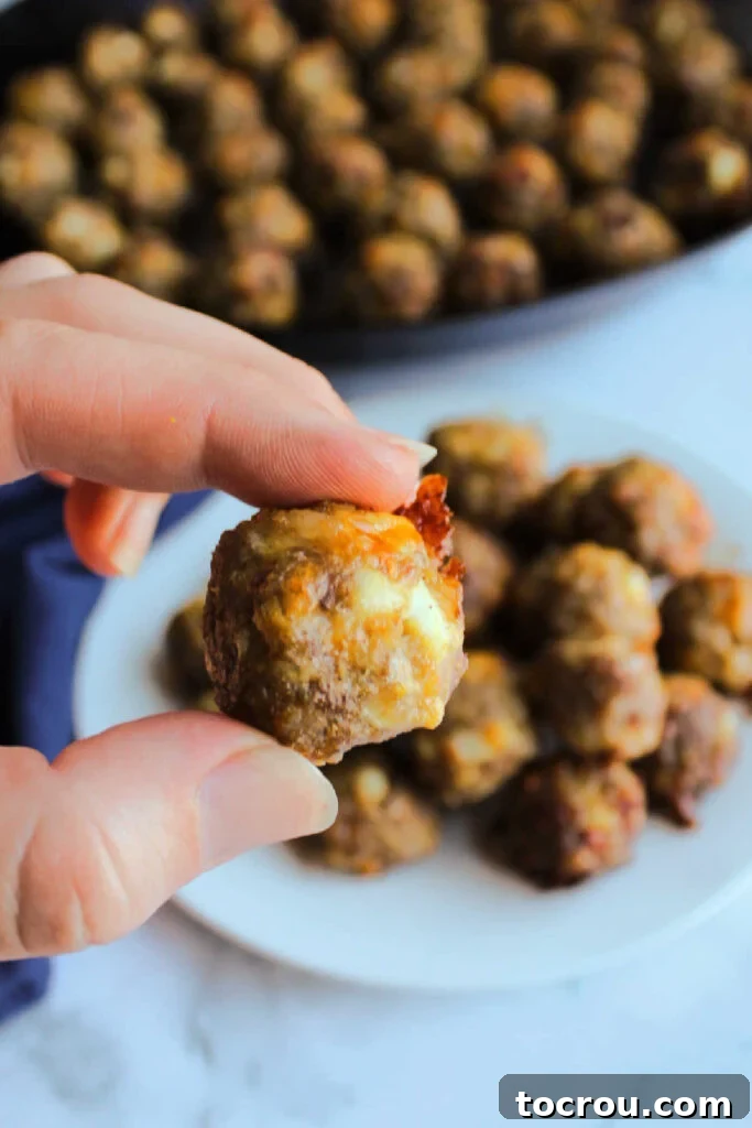 A close-up shot of a hand holding a single, perfectly golden-brown breakfast meatball, showcasing its inviting texture and bite-sized appeal.