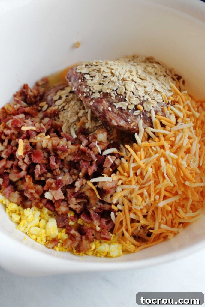 Various breakfast meatball ingredients including chopped hard-boiled eggs, cooked bacon, and shredded cheese, waiting to be mixed in a large bowl.