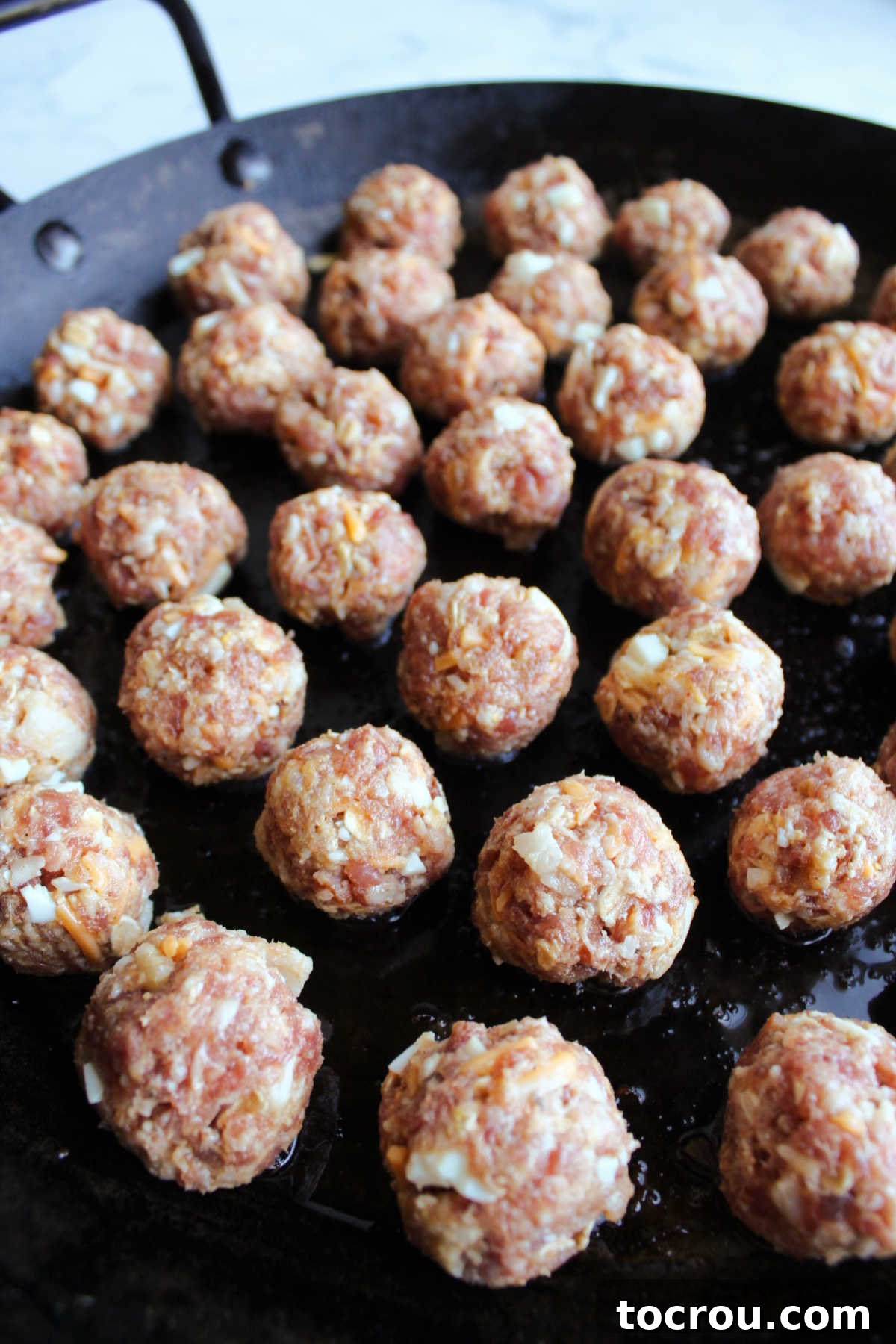A large, black cast-iron skillet brimming with breakfast meatballs, perfectly arranged and ready to be cooked to a golden-brown finish.
