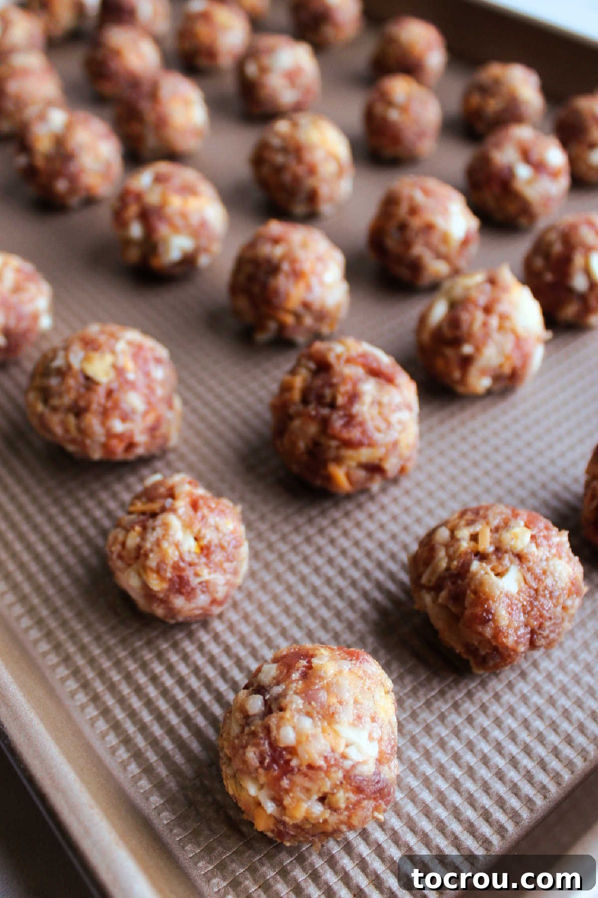 Numerous breakfast sausage meatballs, uniform in size and golden-brown, spread evenly across a sheet pan, just out of the oven and ready to serve.