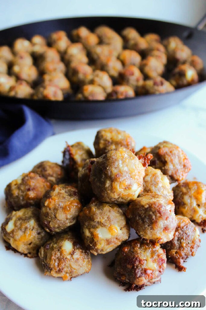 A close-up view of a plate featuring several breakfast sausage meatballs, revealing the delicious internal blend of bacon, eggs, and melted cheese.