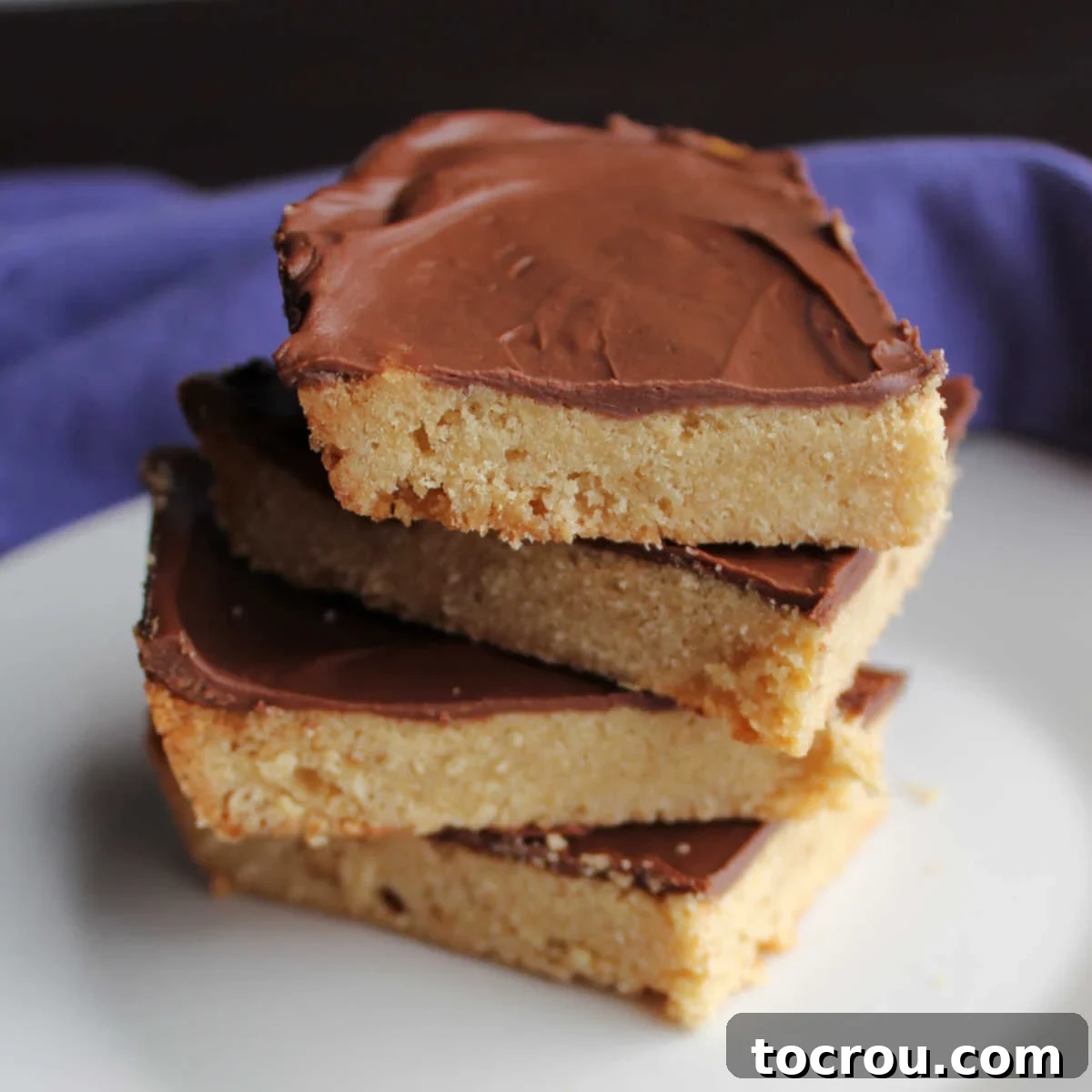A stack of golden brown toffee cookie bars, each generously topped with a melted chocolate layer, resting on a white surface.