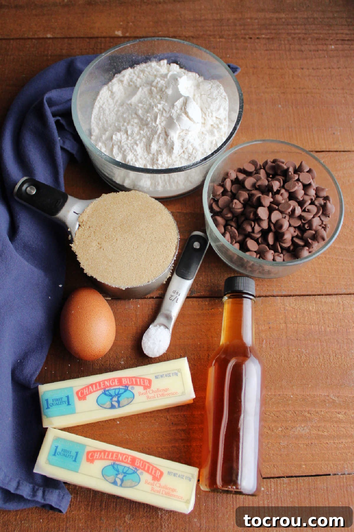 A visual display of the key ingredients for toffee cookie bars: butter, a cracked egg, brown sugar, flour, vanilla extract, salt, and chocolate chips, neatly arranged.