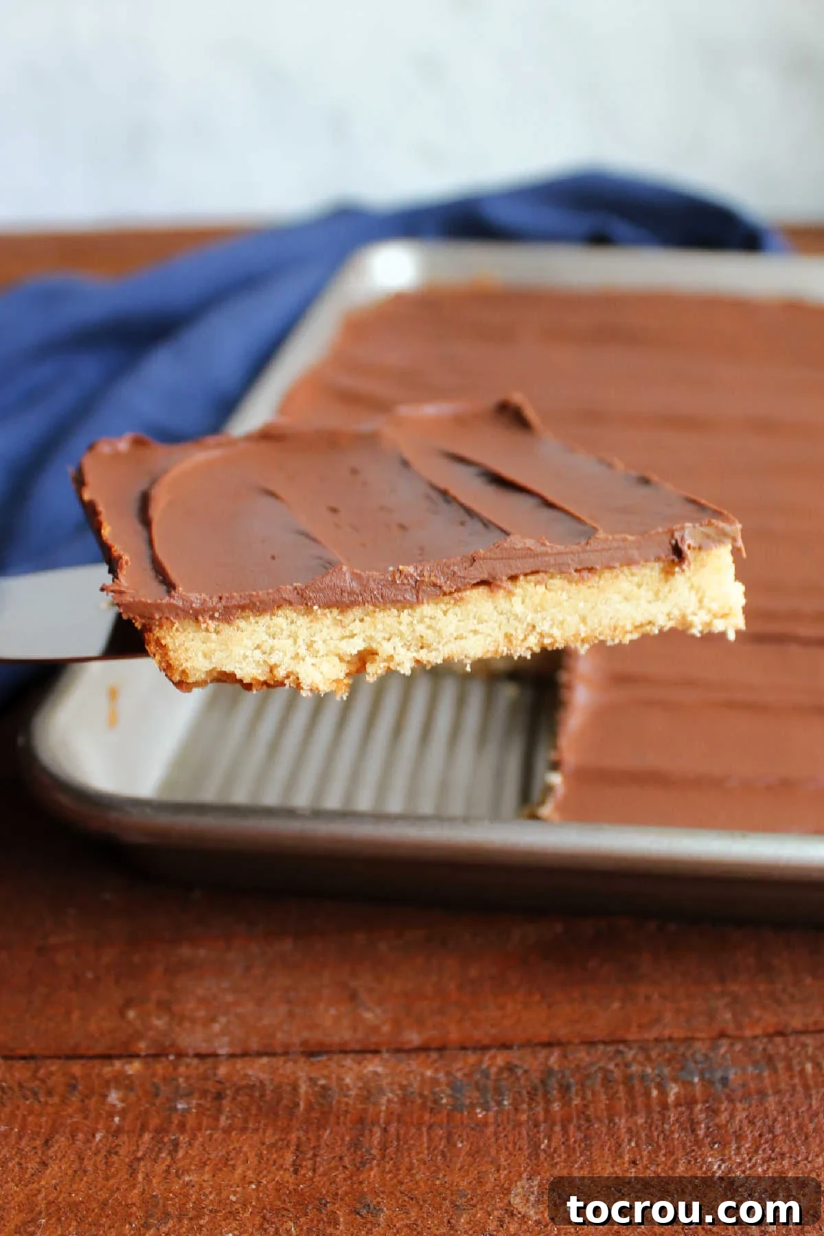 A freshly cut piece of toffee bar being lifted from the pan, showcasing its distinct layers of chewy brown sugar cookie and firm chocolate topping.