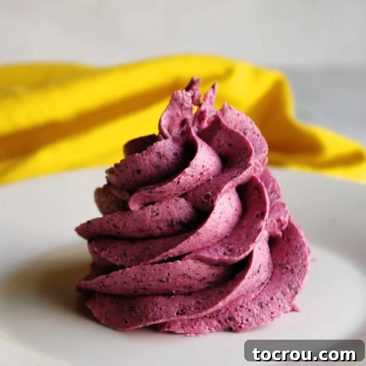 Close swirl of blueberry buttercream showing flecks of berry and deep purple color.