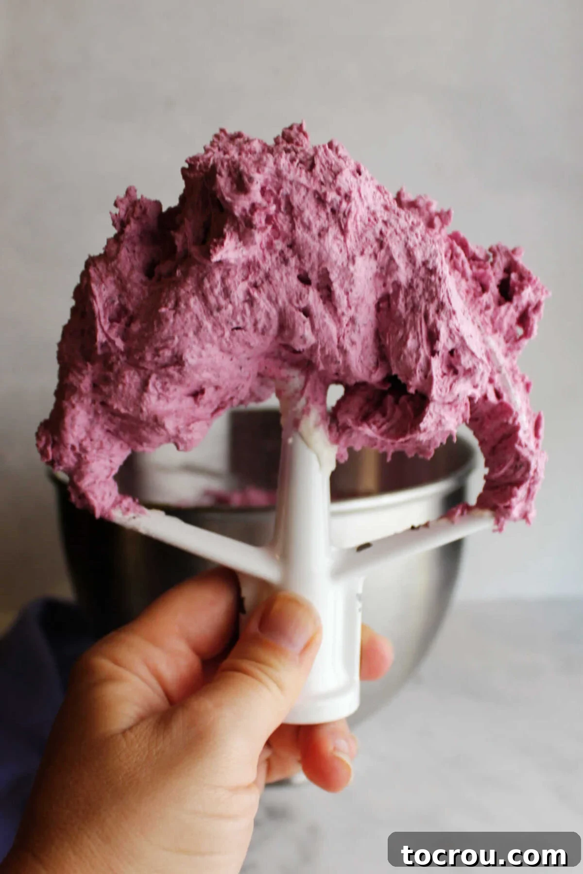 Mixer paddle filled with freshly whipped blueberry buttercream ready to use.