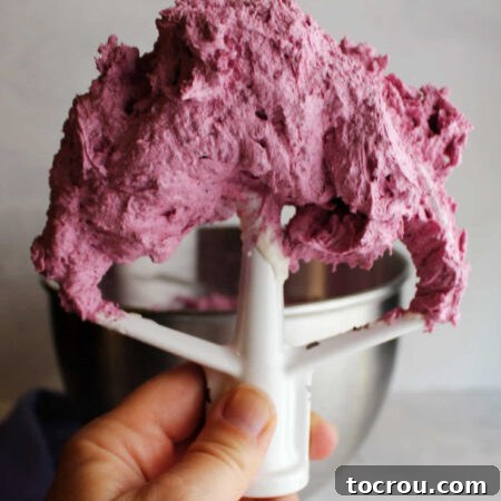Mixer paddle filled with freshly whipped blueberry buttercream ready to use.