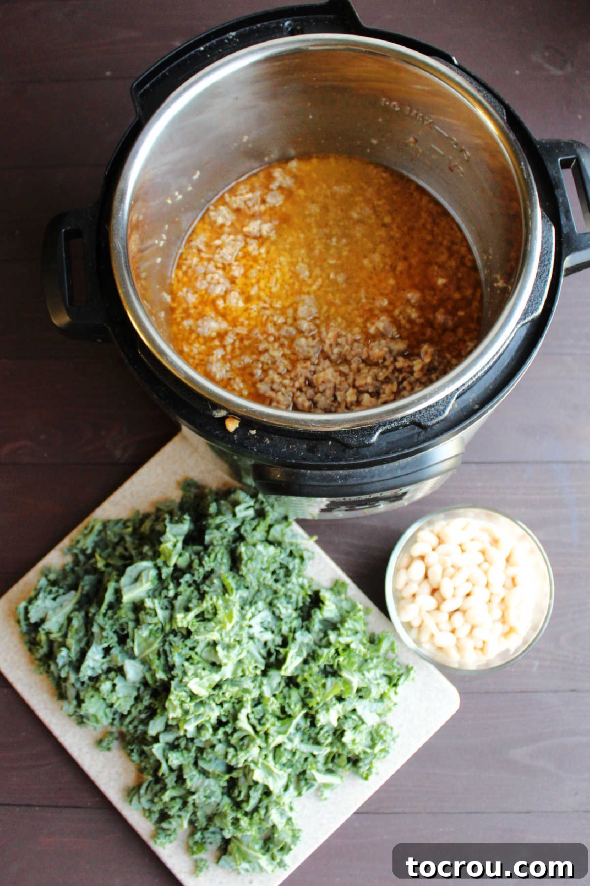 Cooked farro and sausage mixed in the Instant Pot, alongside neatly chopped kale and a bowl of prepared white beans, ready for the next steps.