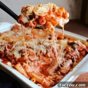 Serving spoon scooping baked ziti out of casserole dish with saucy cheese pulls.