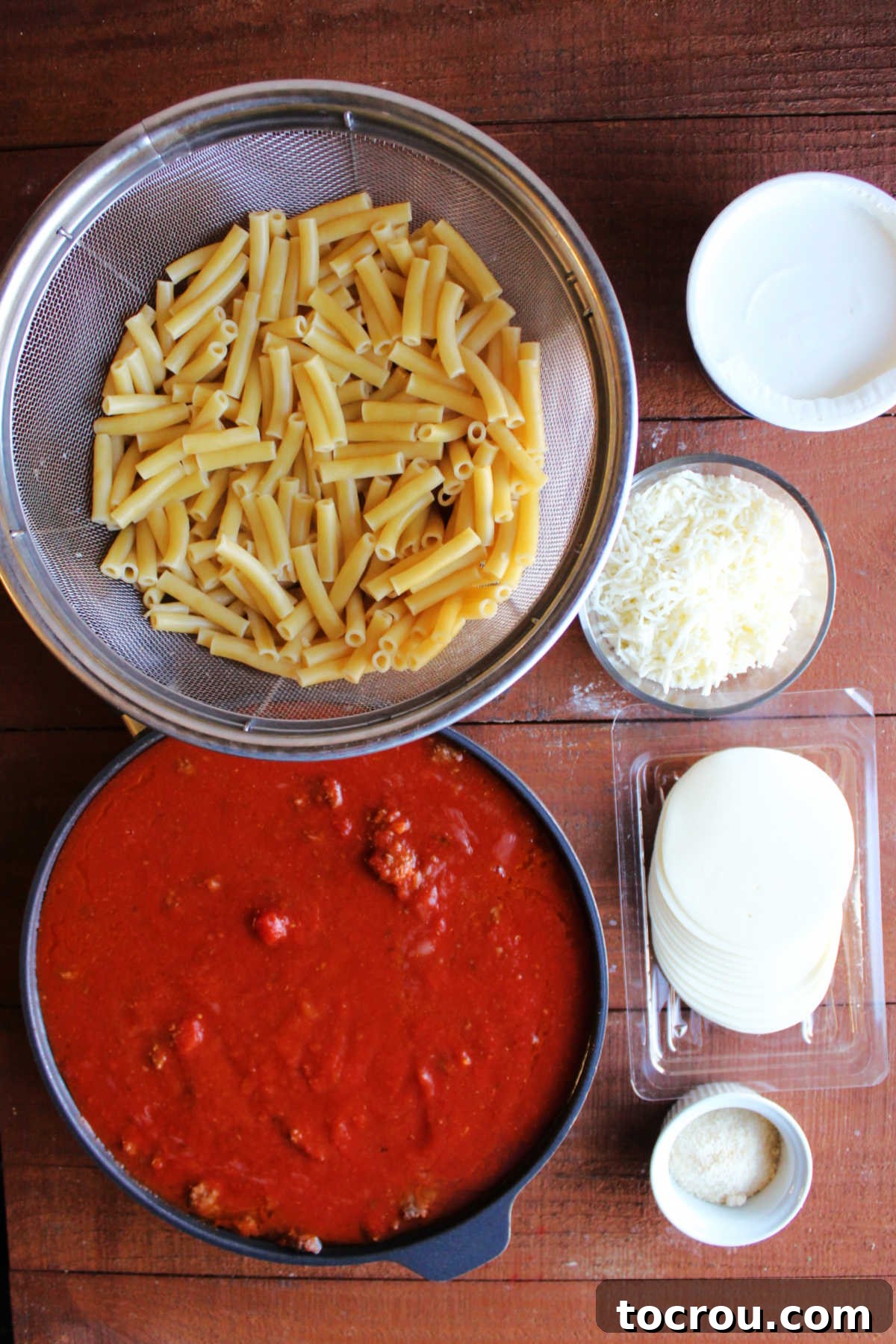 Ingredients for creamy baked ziti casserole, including boiled ziti, sour cream, mozzarella, provolone, Parmesan cheeses, marinara sauce, and browned ground beef.