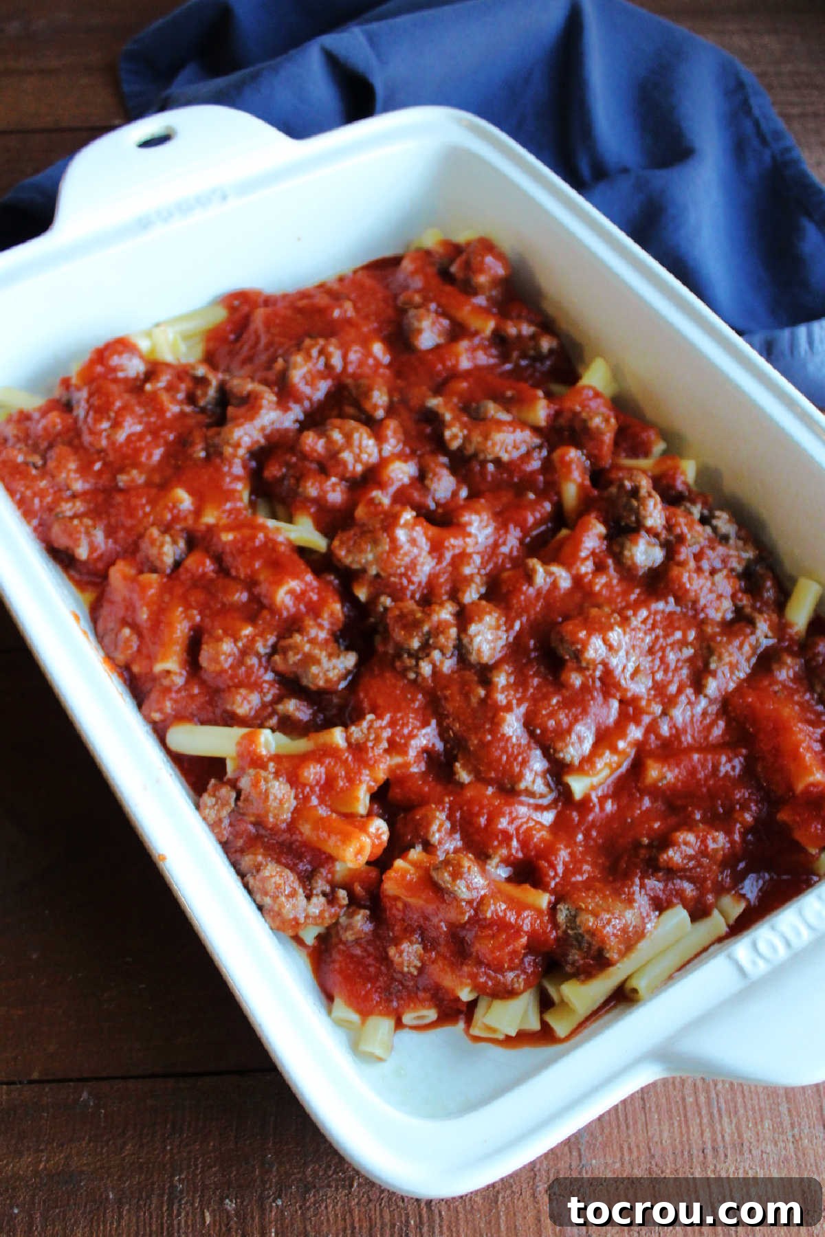First layer of al dente ziti pasta and savory meat sauce in a 9x13-inch baking pan.