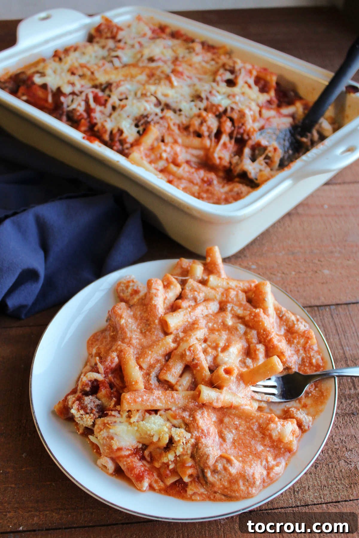 A generous helping of creamy baked ziti on a plate with a fork, perfectly cooked and ready to eat.