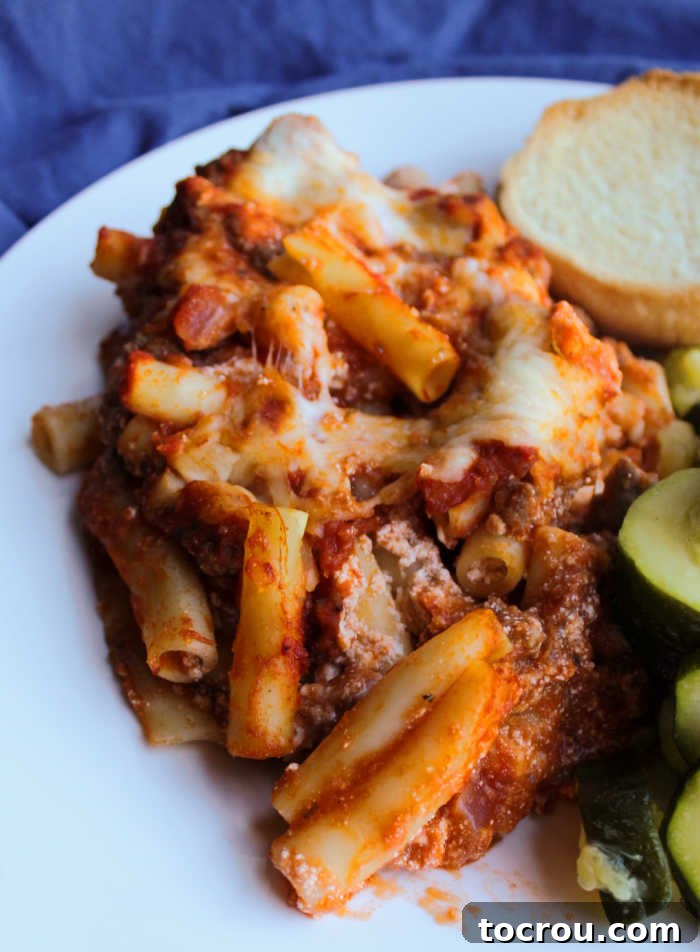 Dinner plate with cheesy baked ziti, accompanied by crispy garlic bread and tender zucchini, creating a complete and satisfying meal.
