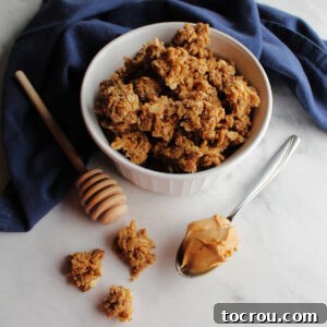 bowl of peanut butter granola next to a spoon of peanut butter and a honey drizzler.