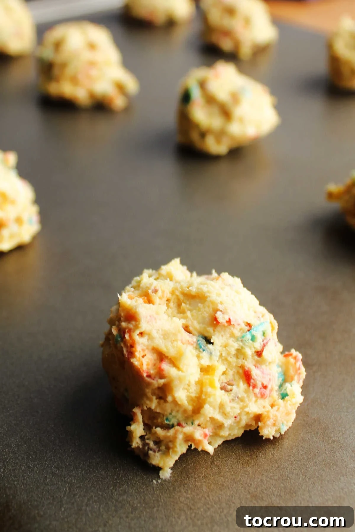 Scooped Fruity Pebbles Cookie Dough Perfectly scooped balls of Fruity Pebbles cookie dough, mixed with colorful cereal and ready for the oven, laid out on a baking pan.