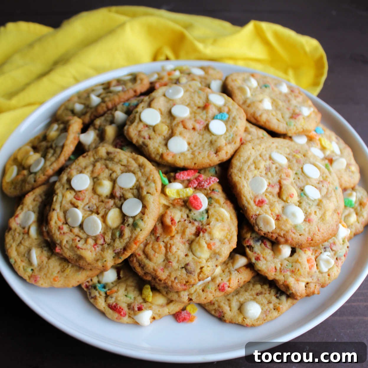 Plate of Fruity Pebbles Cookies A plate generously piled high with colorful Fruity Pebbles cookies, each adorned with creamy white chocolate chips, inviting you to grab one.