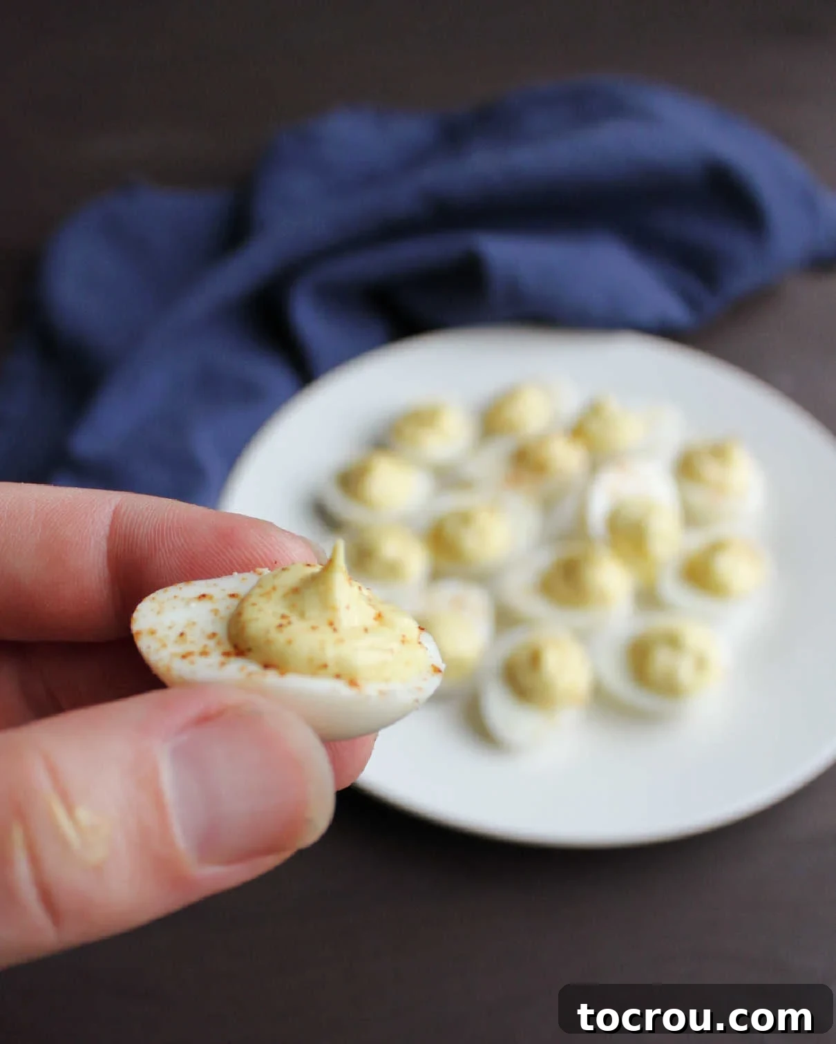 A hand delicately holding a single, perfectly deviled quail egg, showcasing its tiny size and elegant presentation.