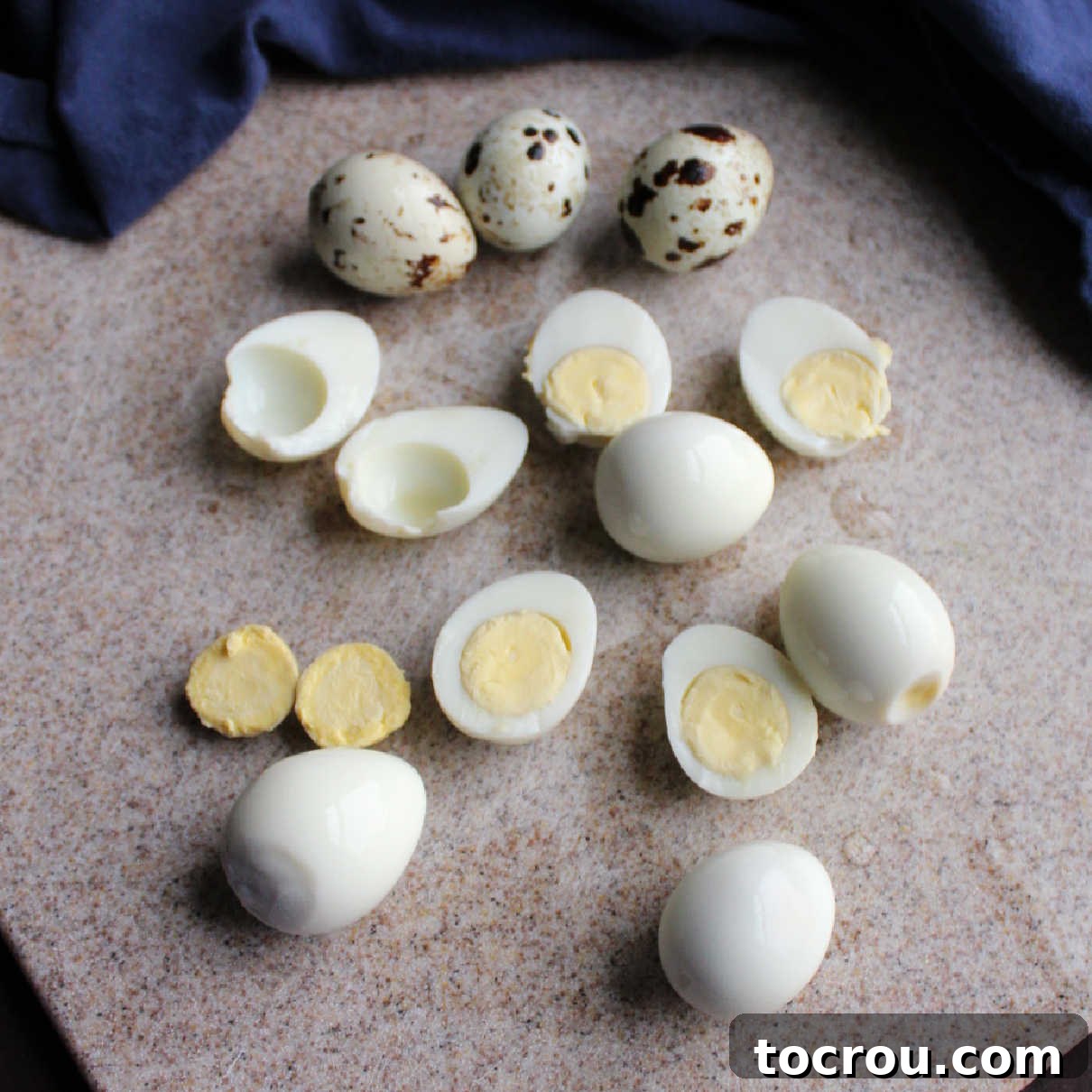 Small, boiled quail eggs carefully cut in half, with some yolks already removed, laid out on a clean cutting board.