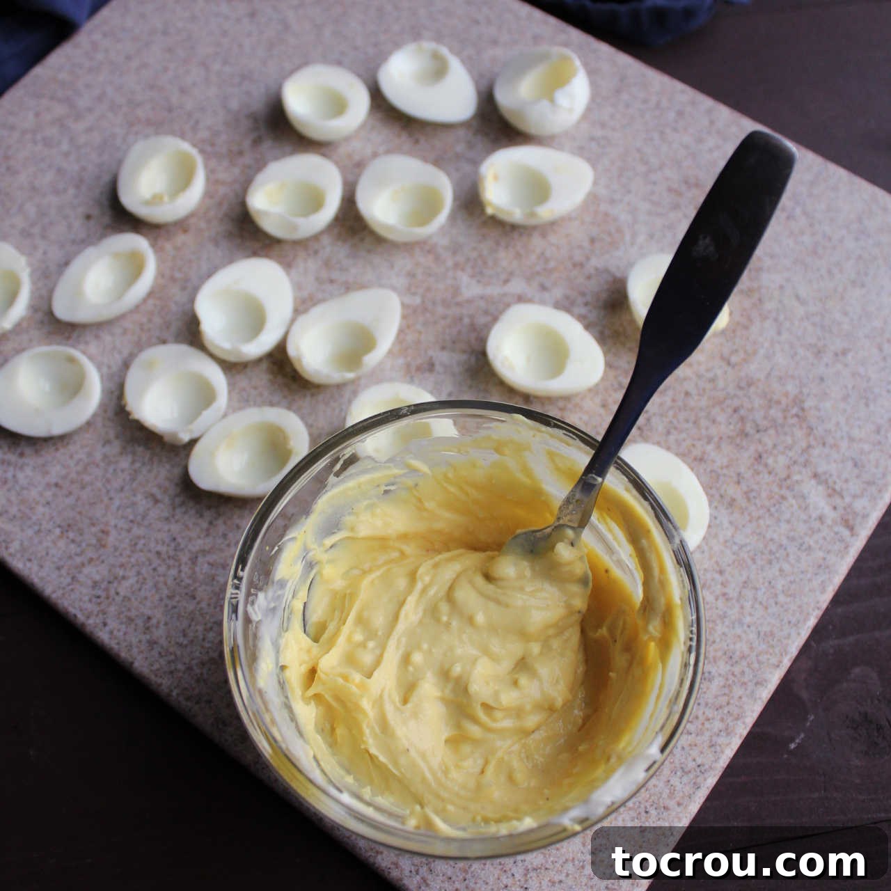 A close-up view of a small bowl filled with creamy, mashed egg yolk filling, positioned beside neatly arranged quail egg halves.