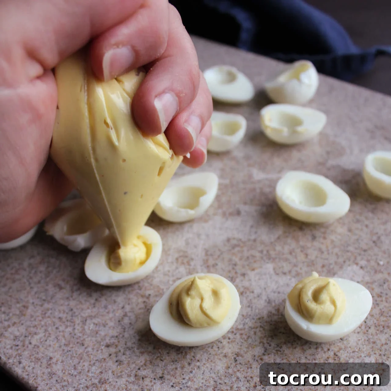 A close-up shot of yellow yolk filling being meticulously piped into the hollowed halves of boiled quail eggs, ready for garnish.