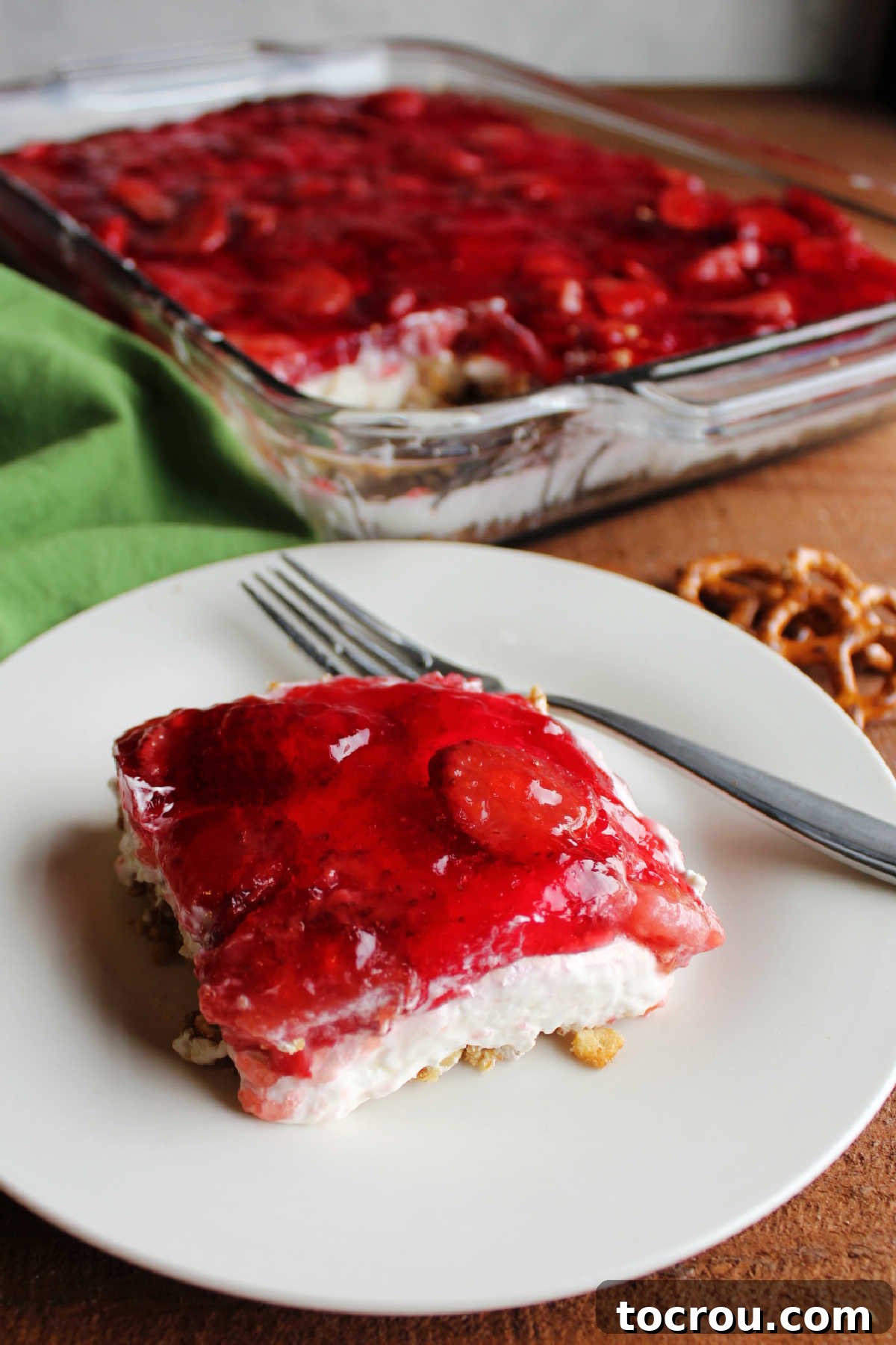 Beautifully Layered Strawberry Pretzel Dessert A perfectly portioned piece of Strawberry Pretzel Salad, clearly showing its distinct layers. The bottom layer is a golden, crunchy pretzel crust, followed by a thick, creamy white cream cheese filling, and topped with a glistening, ruby-red strawberry Jell-O layer embedded with strawberry pieces.