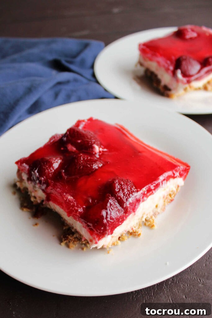 Perfect Slice of Strawberry Pretzel Salad A close-up of a single piece of Strawberry Pretzel Salad, highlighting the crisp, salty pretzel crust, the thick, creamy, cheesecake-like center, and the vibrant, fruit-filled strawberry Jell-O topping.