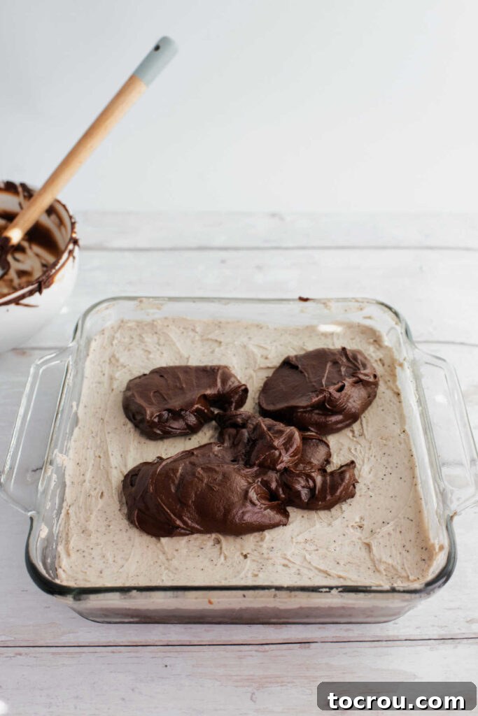 Dollops of warm chocolate ganache on top of coffee buttercream topped brownies, ready to be spread out.
