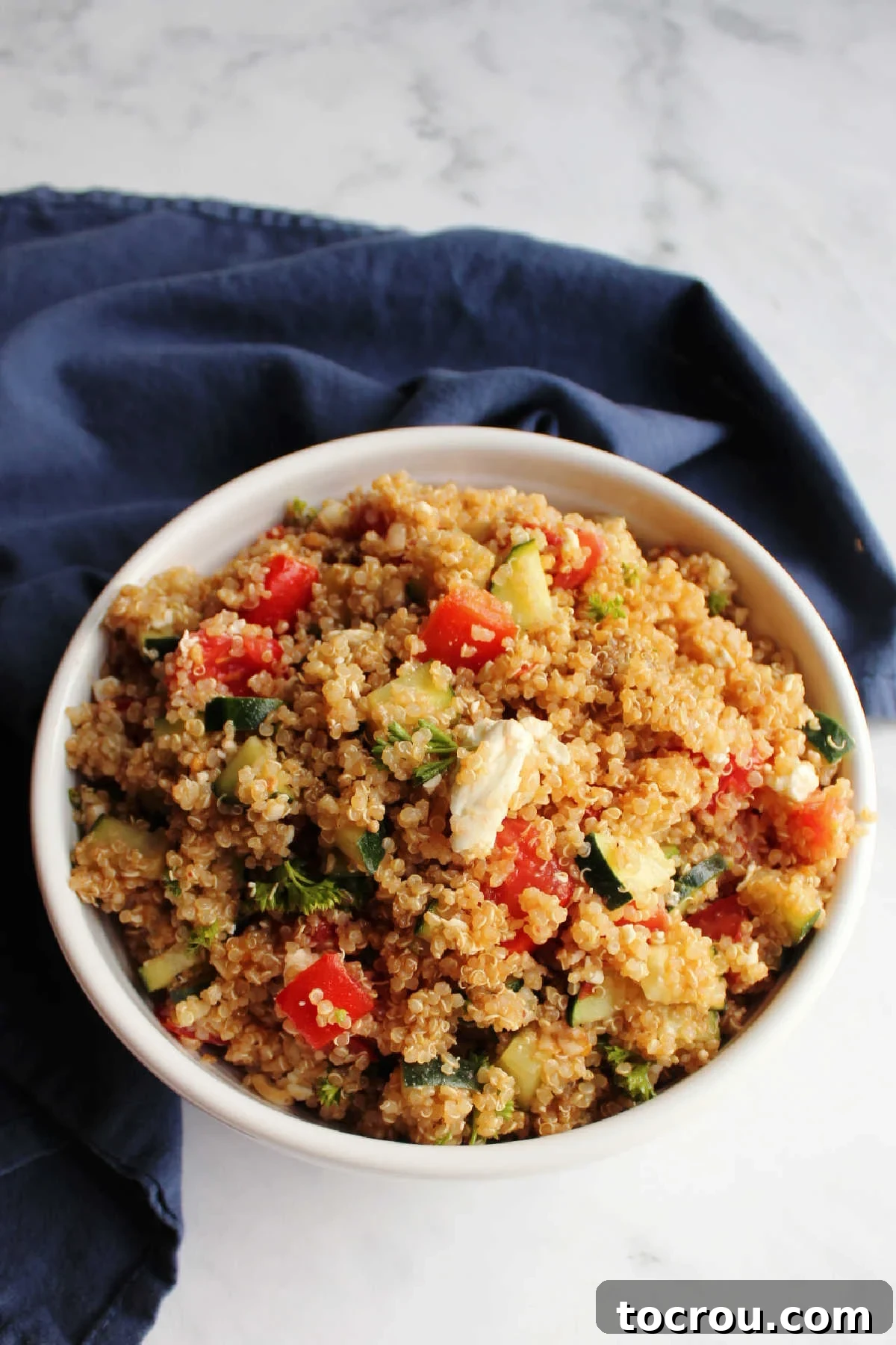 A large, elegant white serving bowl brimming with Mediterranean quinoa salad, showcasing the delightful mix of tomatoes, cucumbers, fluffy quinoa, and crumbled feta cheese.