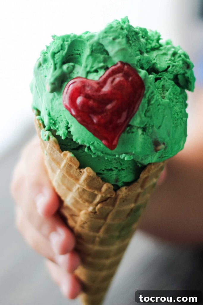 Grinch Ice Cream Cone Child's hand holding ice cream cone filled with green ice cream with red heart to look like the Grinch.