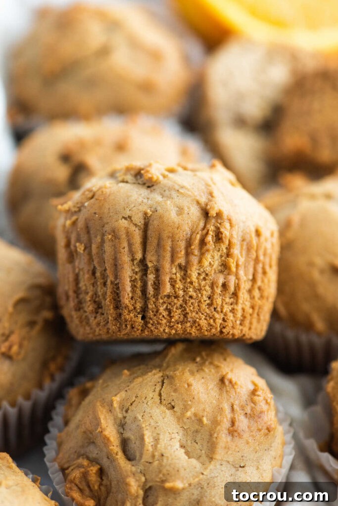 An orange spice muffin with its paper wrapper removed, revealing its golden-brown exterior, ready to be eaten.