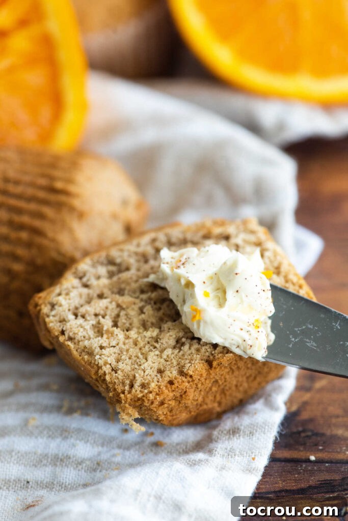 A knife with orange honey butter on it, ready to be spread over an orange cinnamon muffin.