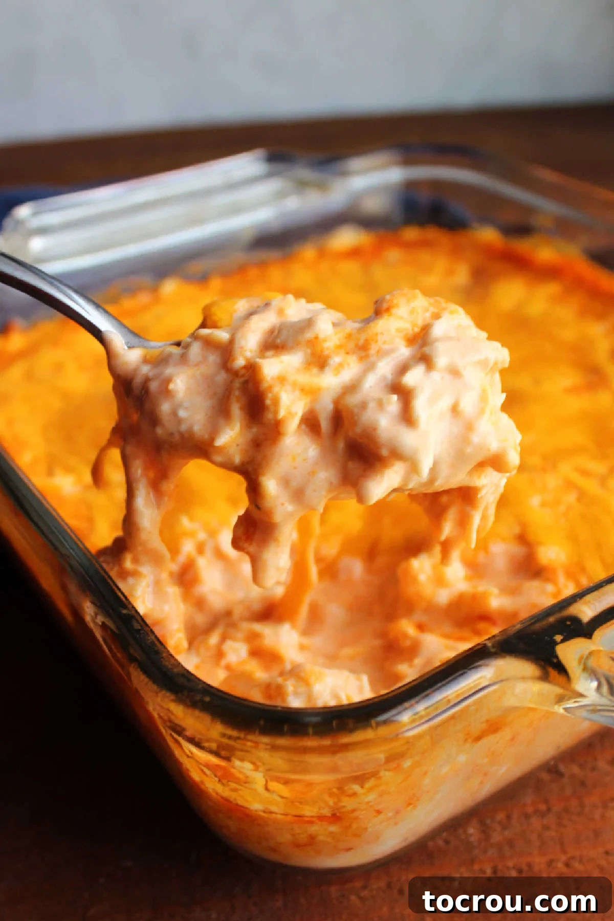 Ultimate Creamy Buffalo Chicken Dip 7 A serving spoon lifting a generous portion of hot, gooey buffalo chicken dip from a baking pan, showing its rich, melted cheese and shredded chicken texture, ready to be enjoyed.