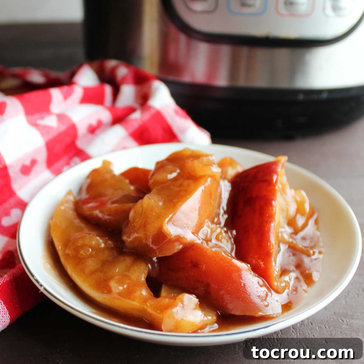 Bowl of apples coated in thick sweet cinnamon mixture in front of instant pot.