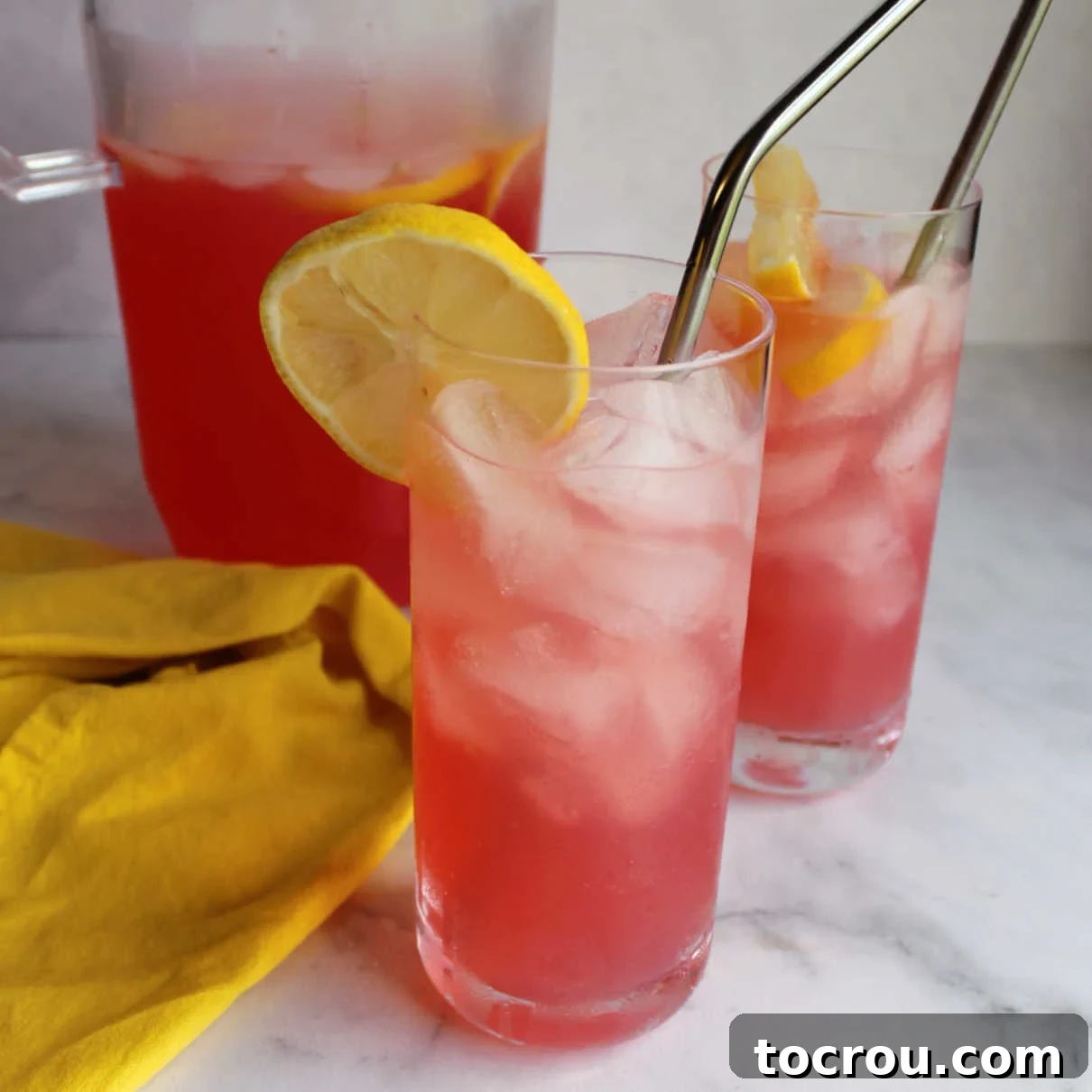 Glasses of homemade pink lemonade on ice, garnished with fresh lemon slices and mint sprigs.