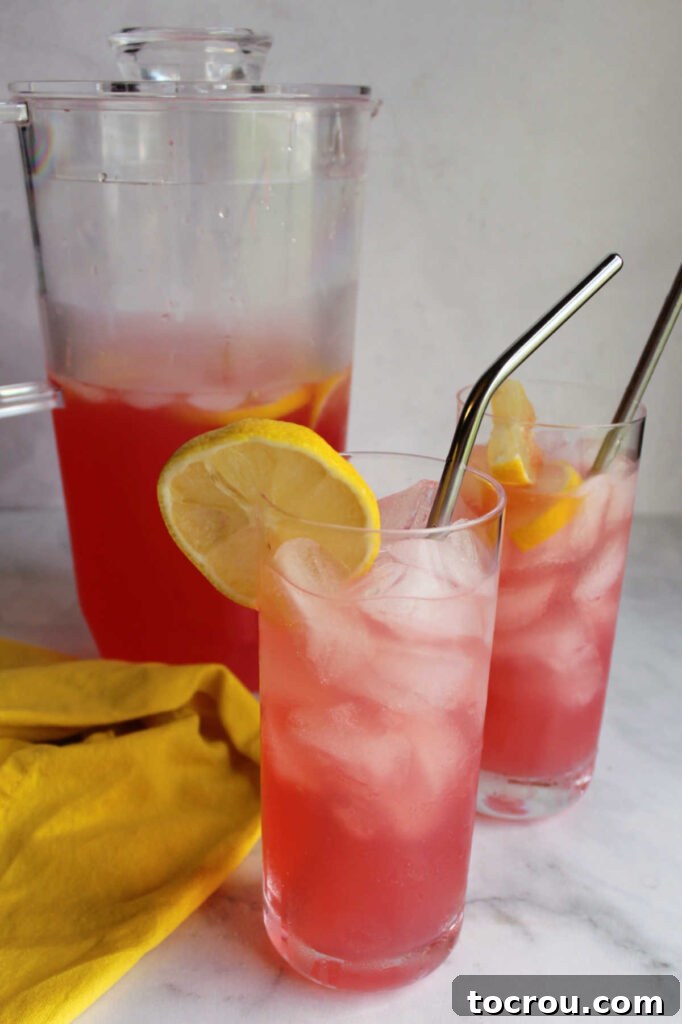 Glasses of freshly made pink lemonade with ice and lemon slices on a rustic wooden table.