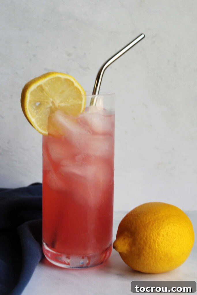 Tall glass filled with homemade pink lemonade and ice, placed beside a fresh whole lemon and a sprig of mint.