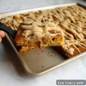 Spatula lifting slice of peach sheet cake out of pan showing chunks of fruit in cake and drizzled brown butter icing on top.