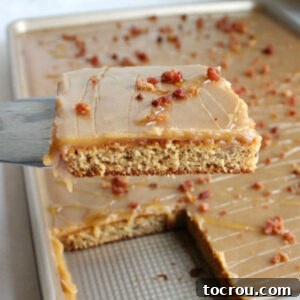 close shot of first slice of elvis sheet cake being lifted out of sheet pan showing moist banana cake, smooth peanut butter icing and crumbles of cooked bacon.