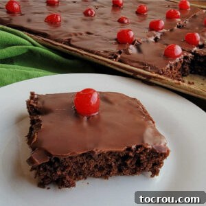Piece of chocolate cherry sheet cake with chocolate icing and a maraschino cherry on top.