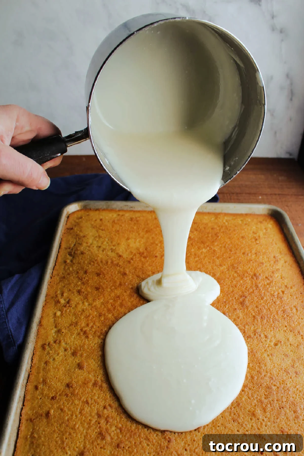 11 Must-Try Texas Sheet Cake Recipes 5 Pouring warm vanilla icing out of saucepan and onto baked vanilla Texas sheet cake.