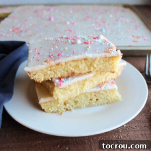 Slices of vanilla Texas sheet cake topped with vanilla icing and sprinkles stacked on top of each other showing buttery cake texture.