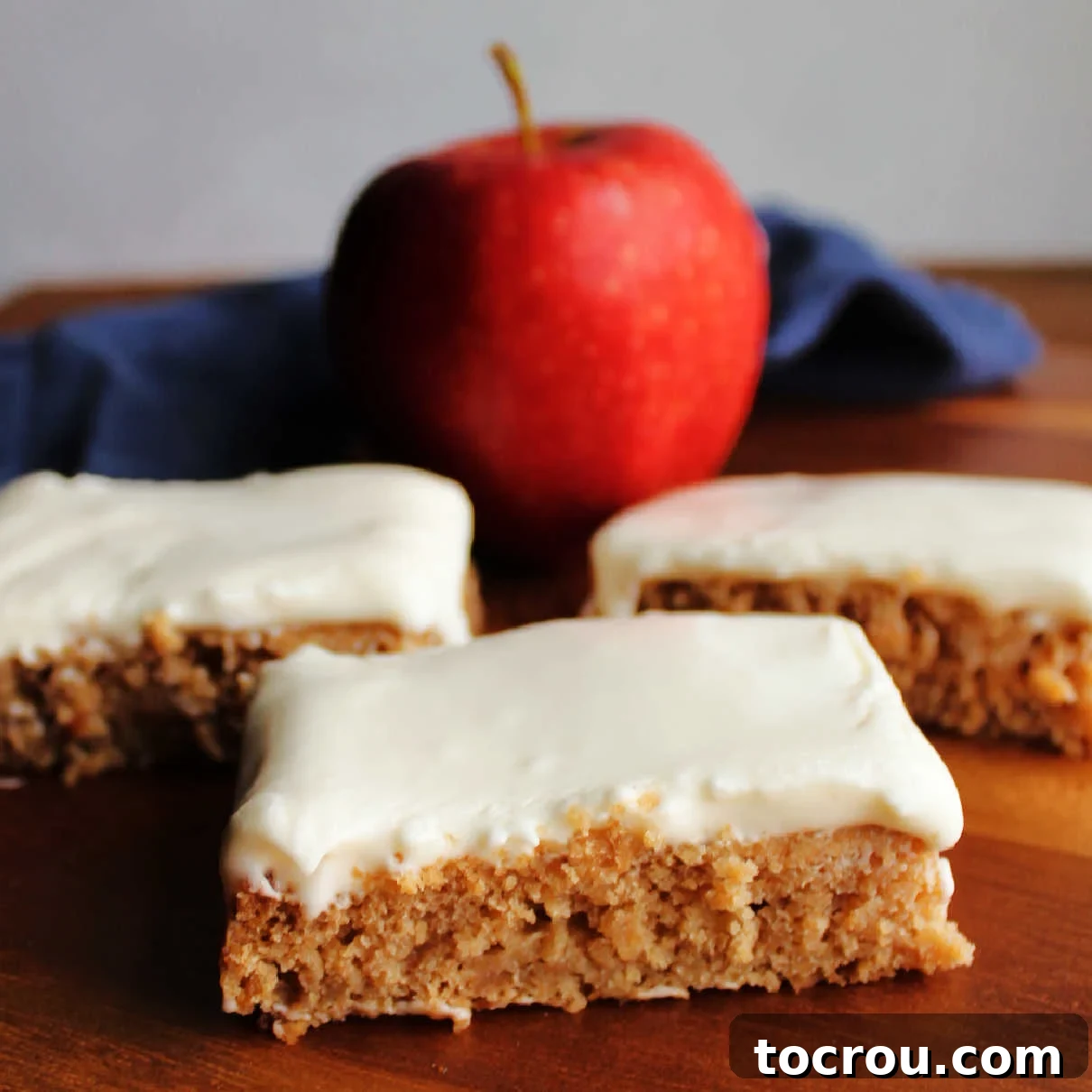 Spiced Applesauce Bars with Tangy Cream Frosting 2 Pieces of applesauce cake topped with soft white sour cream frosting with an apple in the background.