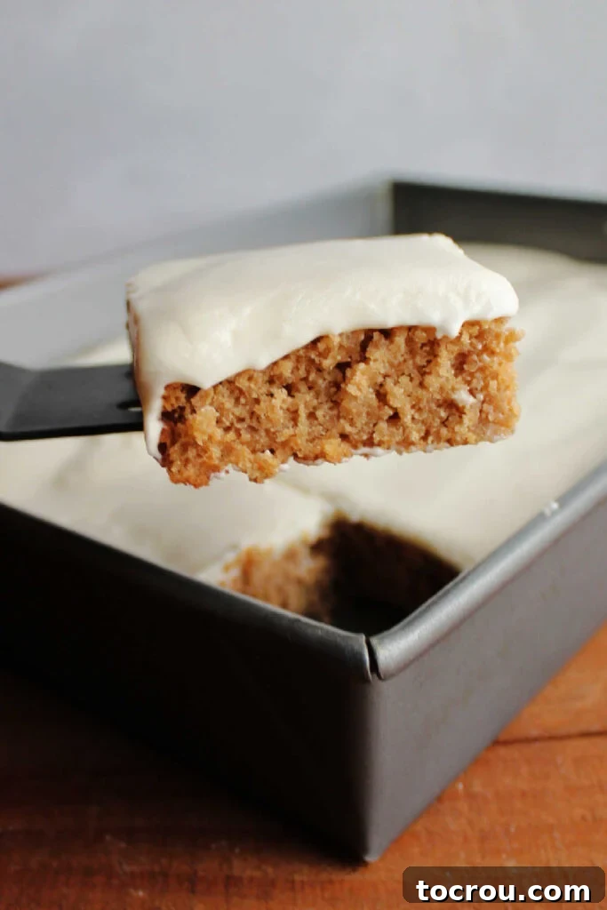 Spiced Applesauce Bars with Tangy Cream Frosting 7 Lifting piece of applesauce bars topped with sour cream frosting out of pan.