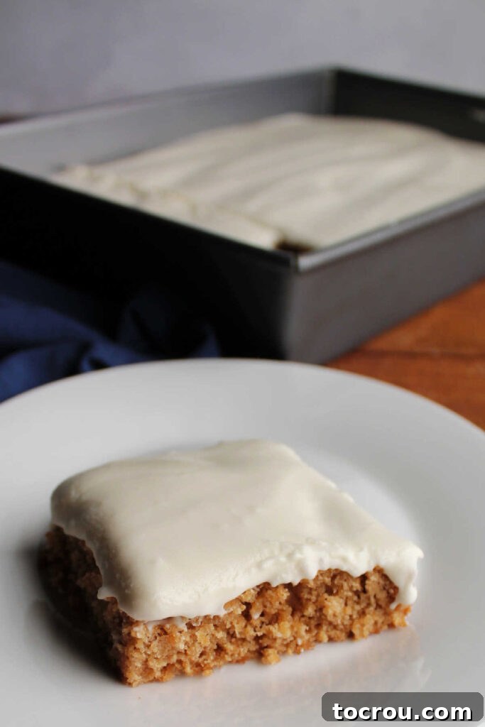 Spiced Applesauce Bars with Tangy Cream Frosting 8 Piece of cakelike applesauce bar on plate in front of pan of sour cream frosting topped dessert in background.
