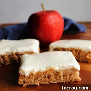 Spiced Applesauce Bars with Tangy Cream Frosting 9 Pieces of applesauce cake topped with soft white sour cream frosting with an apple in the background.