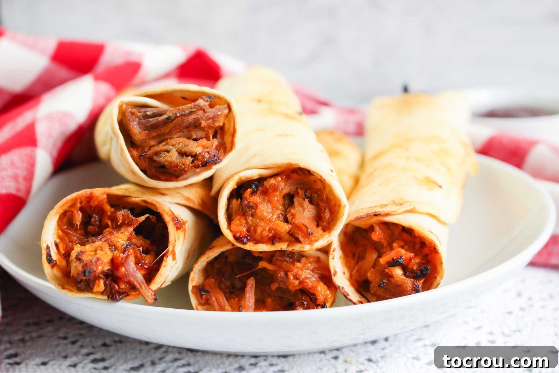 Crispy Air Fryer Pulled Pork Taquitos Plate of golden-brown air-fried taquitos filled with BBQ pulled pork and melted cheese, ready to be enjoyed.