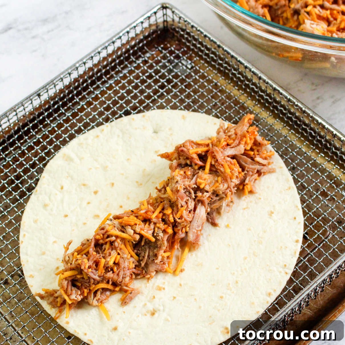 Preparing Pulled Pork Taquitos A fajita-sized tortilla with a generous line of BBQ pulled pork and cheese down the center, ready to be rolled into a taquito.
