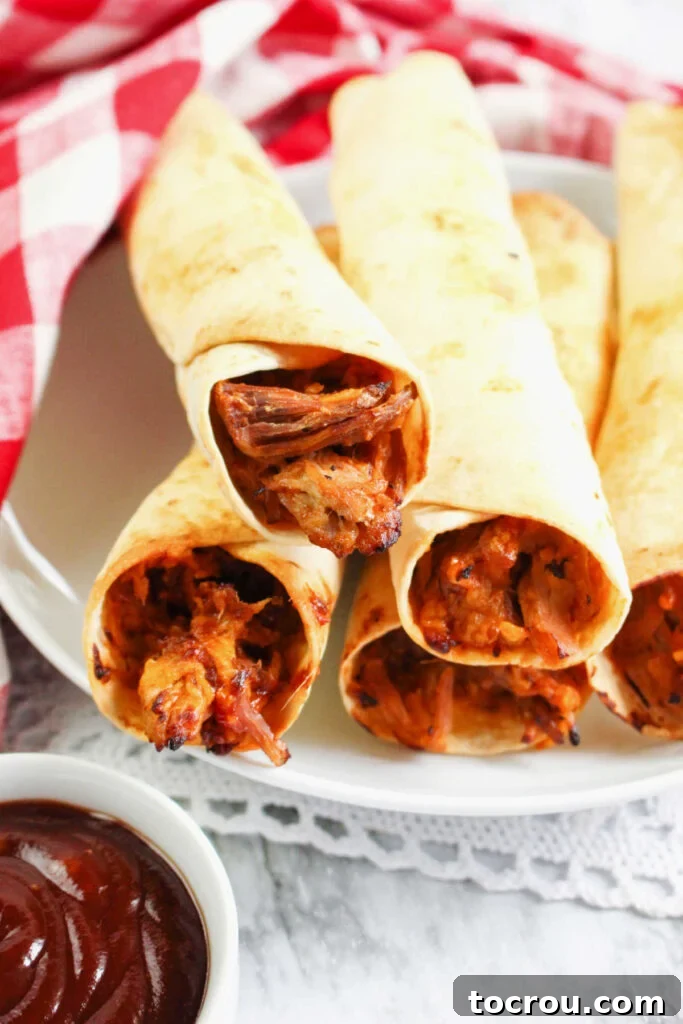 Pulled Pork Taquitos with Dip A plate of crispy air-fried pulled pork taquitos served with a small bowl of BBQ sauce for dipping.